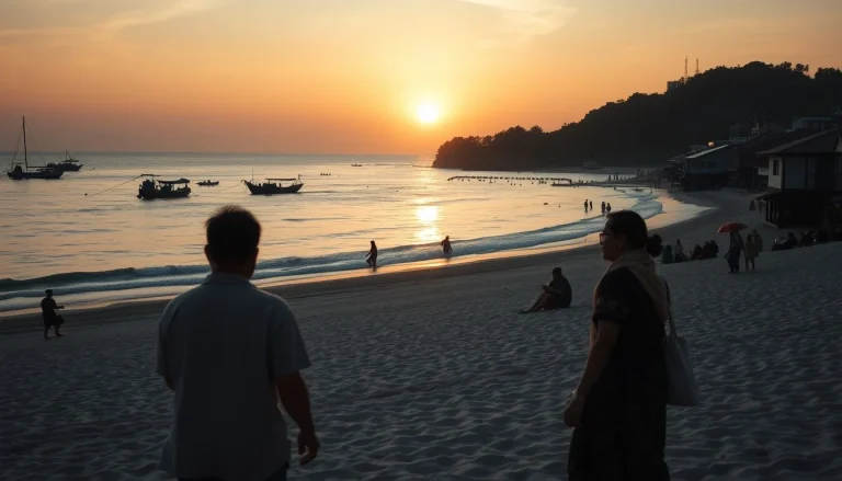 A wide tropical beach at sunset with small boats offshore, people along the shore, and simple buildings beneath a wooded
