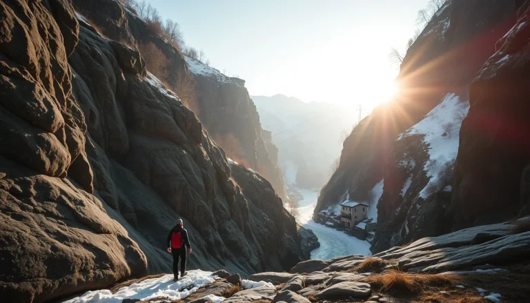 A lone hiker in dark clothing with a red backpack walks through a snowy rocky gorge above a pale, partly frozen river, with