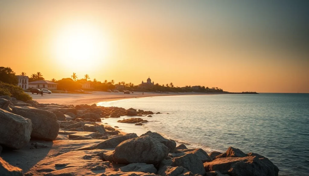 A rocky tropical shoreline at sunset with calm turquoise water, palms, low buildings, vehicles, and a prominent domed